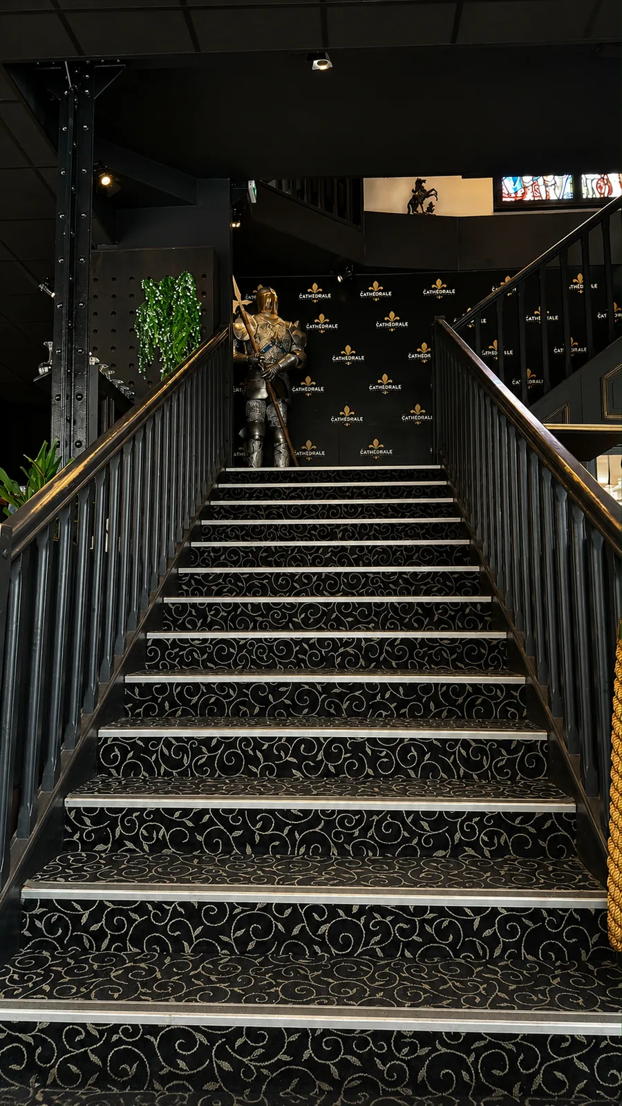 Escalier menant à l'étage, gardé par une armure devant le mur aux fleurs de lys